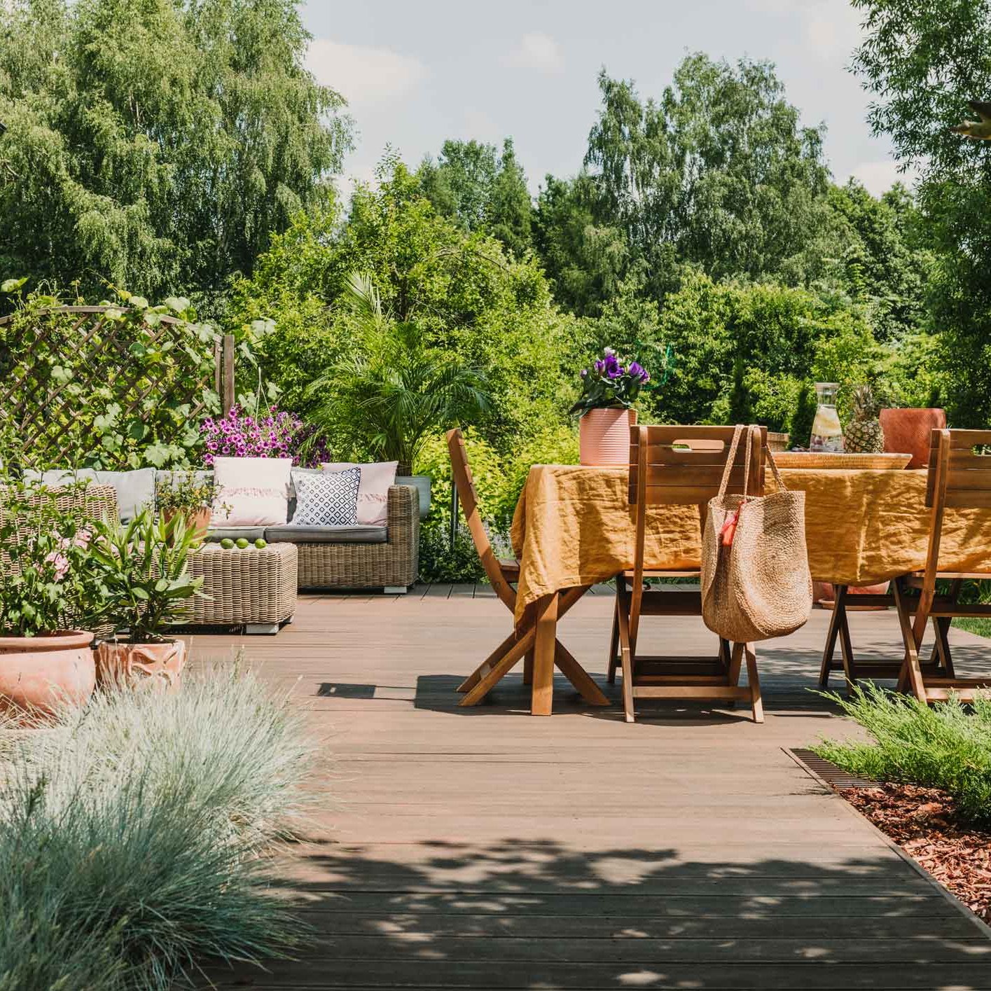 Gartenmöbel aus Holz stehen auf Holzterrasse in einem Garten mit vielen Bäumen und anderen Pflanzen